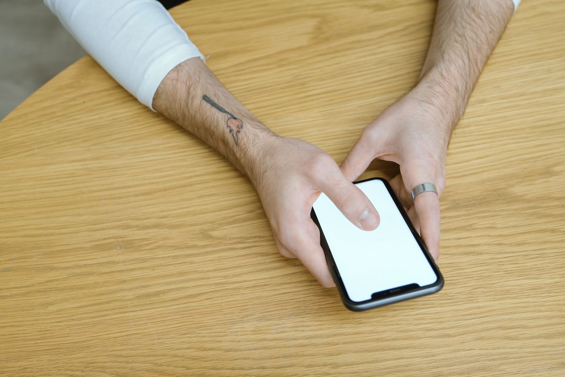Dłonie trzymające telefon przy drewnianym stole, zdjęcie ilustracyjne